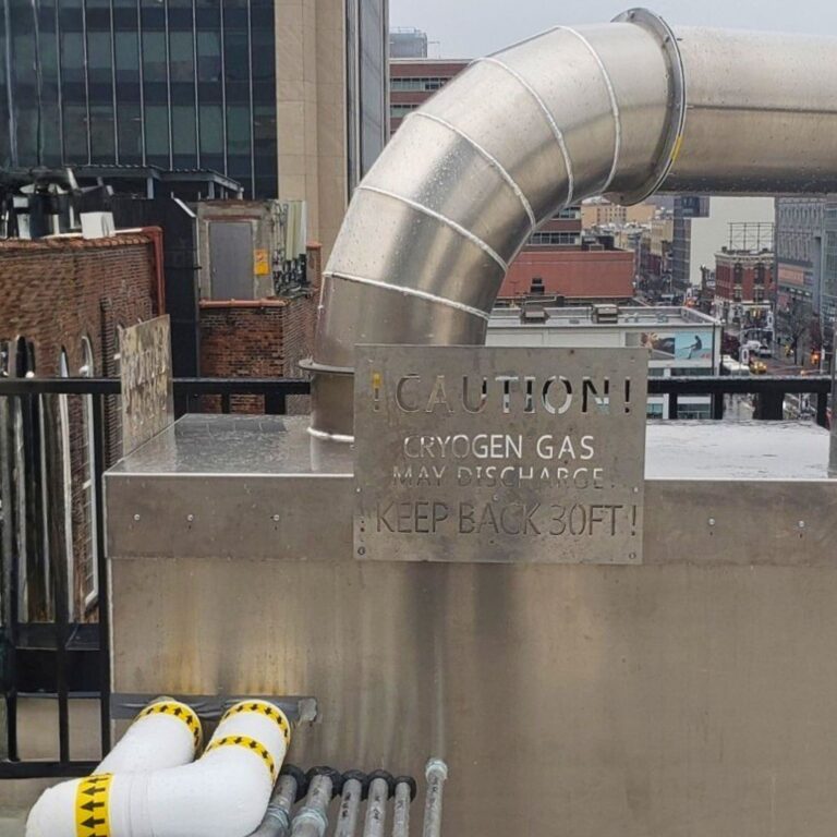 Stainless steel cryogen exhaust vent on rooftop with required warning sign for gas discharge safety.