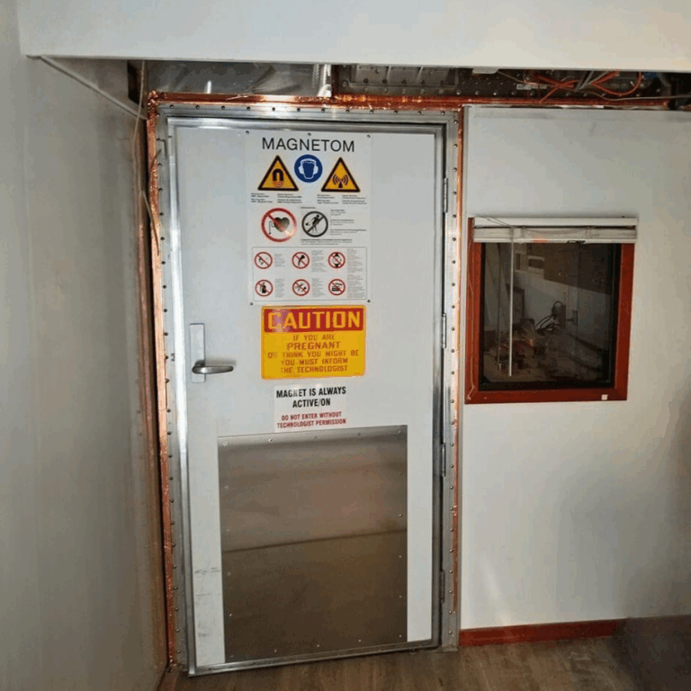 MRI room door featuring exposed copper RF shielding tape around the frame and safety signage.