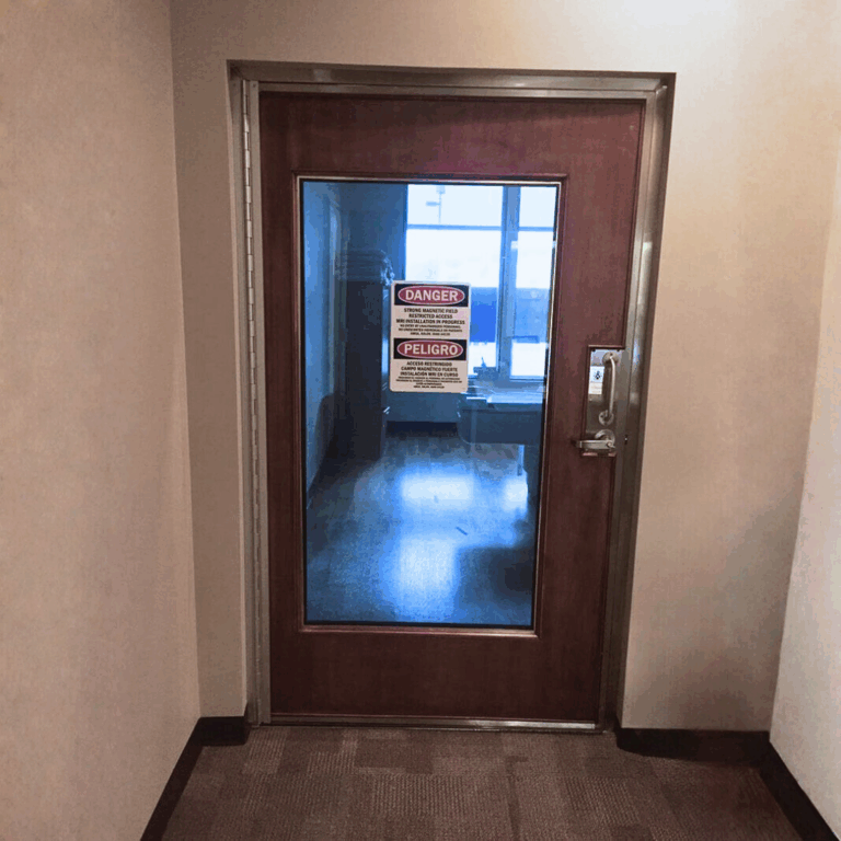 RF shielded entrance door with full window and magnetic field safety warning signage.