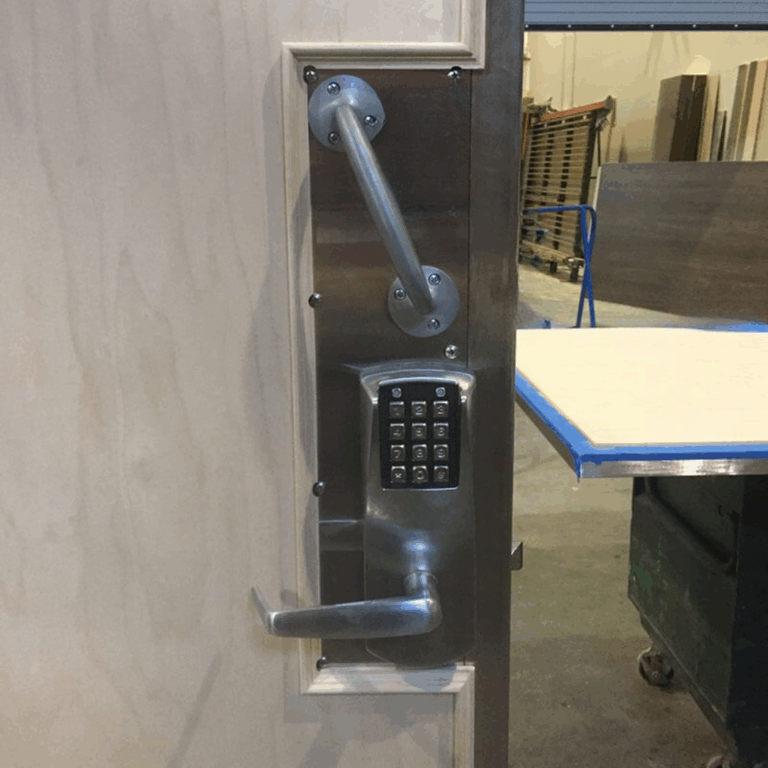 Security close up of non ferrous hardware, pull bar, and keypad lock on a light wood MXR door.