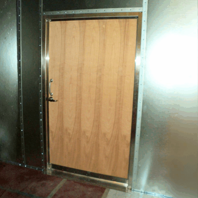 Finished dark wood shielded door installed next to galvanized modular RF shielding panels on site.