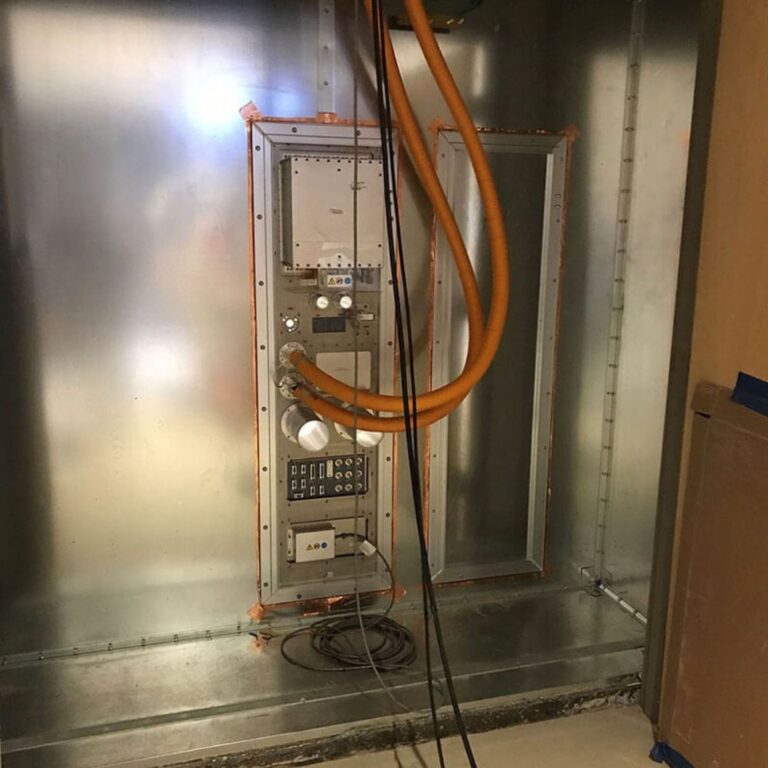 MRI RF equipment rack (enclosure) installed in the shielded room wall with large orange RF cables connected.