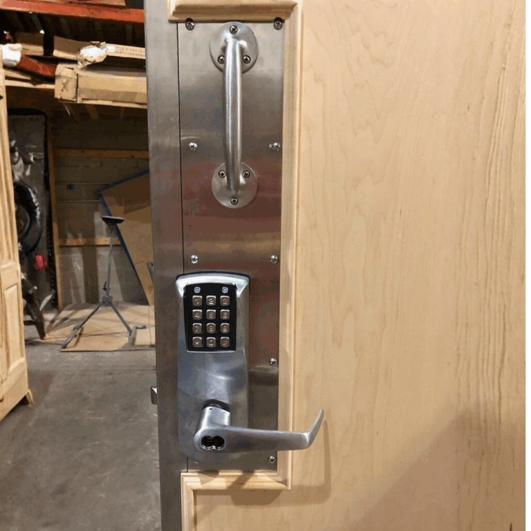 Security close up of non ferrous hardware, pull bar, and keypad lock on a light wood MXR door.