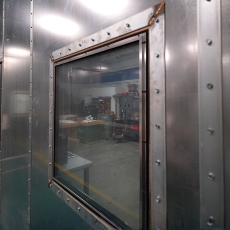 Square RF shielded window with riveted border installed in a galvanized steel shielding wall.