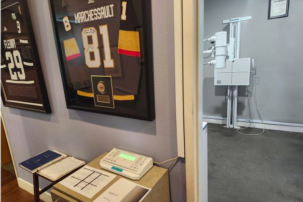 Chiropractic office featuring framed hockey jerseys and an X ray machine in the clinical exam room.