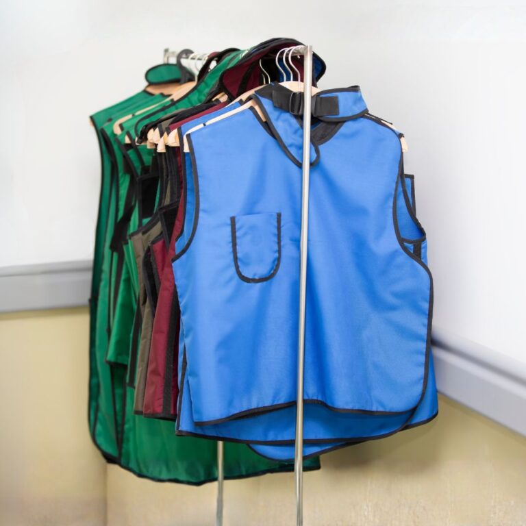 Close up showing the detail, colors (blue, green, maroon), and protective collars of medical lead aprons on hangers.