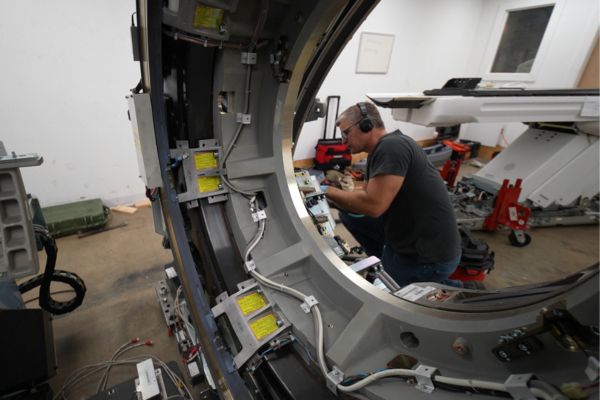 Service technician repairing internal components of medical CT scanner imaging system.