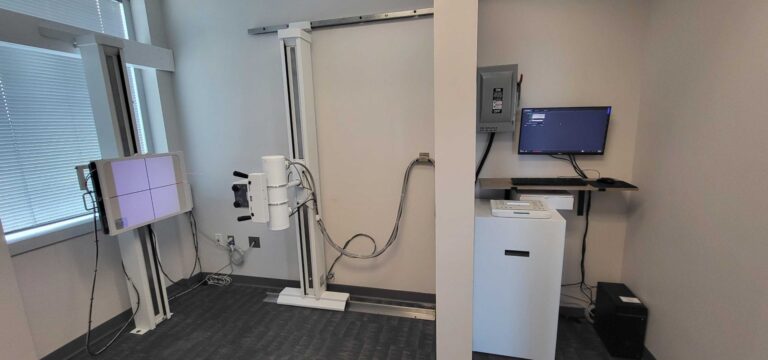 Digital chiropractic X ray room with vertical Bucky stand and lead shielded technician station.