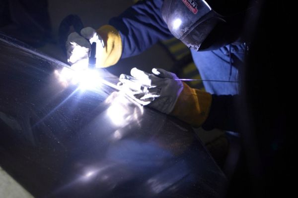 Industrial worker performing shielded metal arc welding on steel using protective face shield and safety gloves.