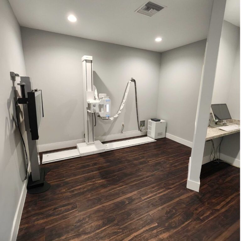 A clean and modern orthopedic X ray room featuring a digital radiography machine and a wall mounted imaging station in a professional medical office.