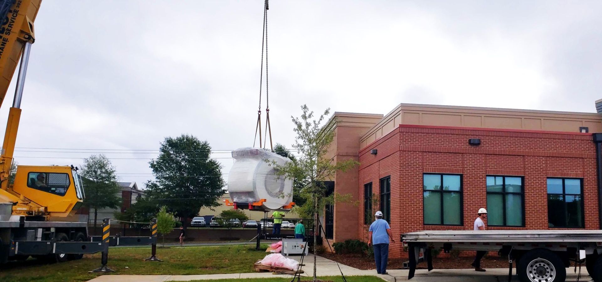 Construction team in hard hats hoisting a large GE MRI scanner into a building opening during medical equipment installation.