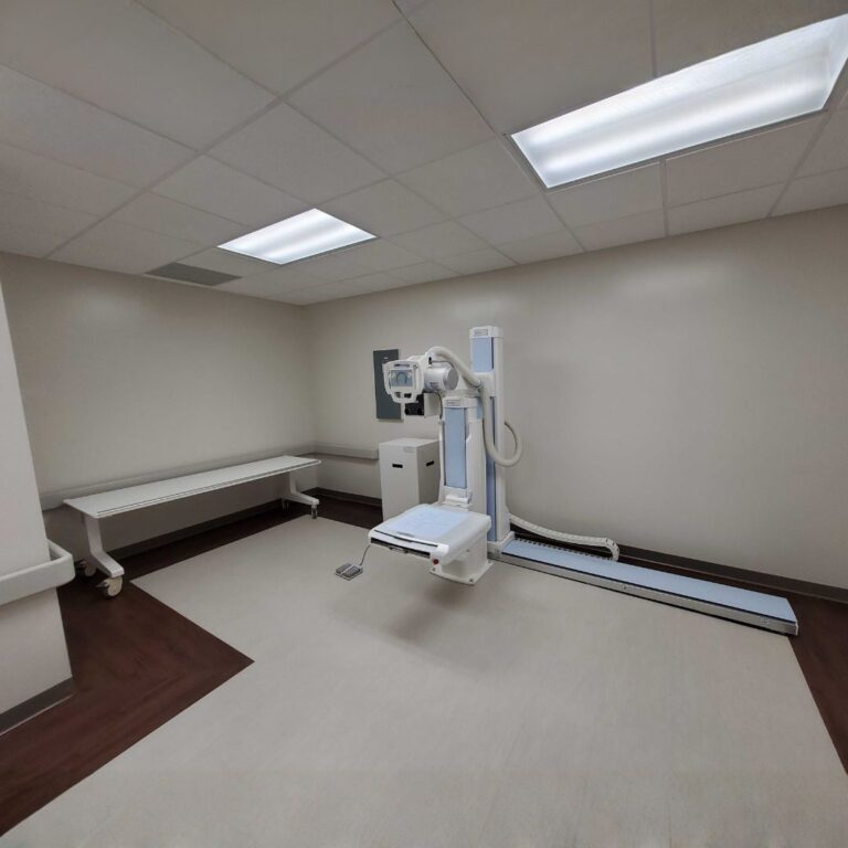 Floor-rail X-ray system being installed in a large clinical room with dark trim.