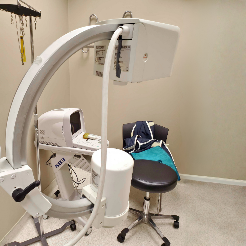 Portable C-arm X-ray machine and fluoroscopy equipment in a medical diagnostic imaging room.