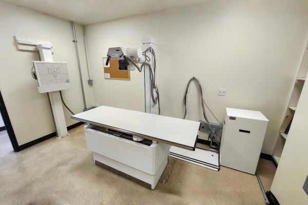 A fully assembled X-ray system in a clinical room with a bulletin board prior to relocation.
