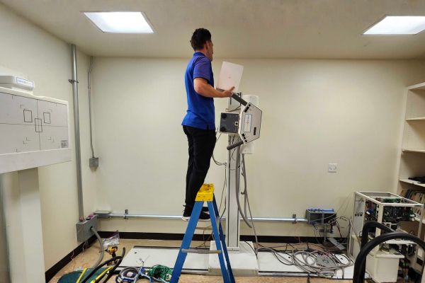 A technician on a ladder dismantling X-ray equipment components in a clinic.