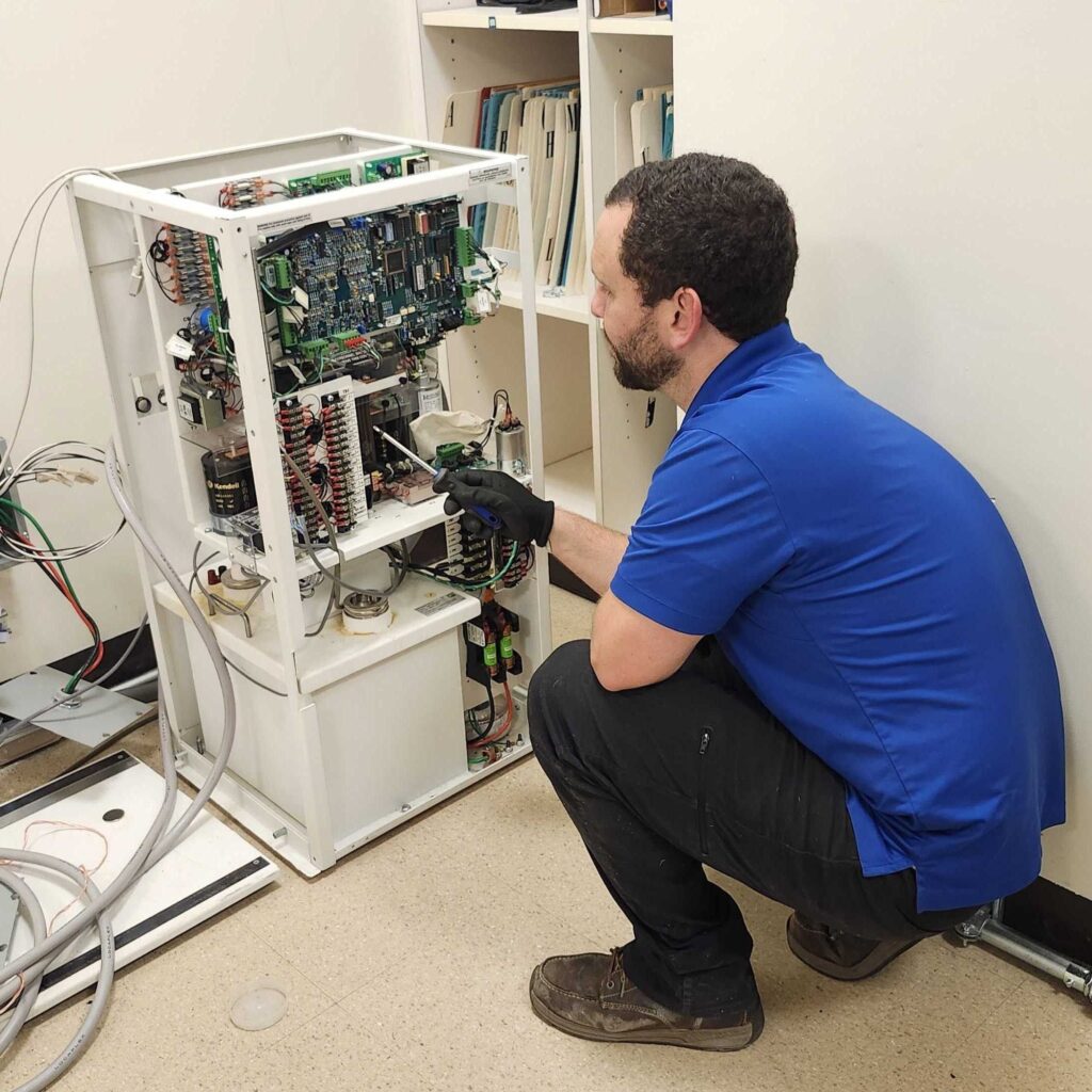 A technician in a blue shirt inspects the internal circuitry of an X-ray generator during deinstallation.